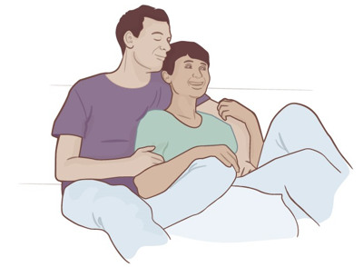 En man och en kvinna sitter ner bredvid varandra, mannen håller om kvinnans axel och kvinnan vilar sin underarm på mannens lår och knä.